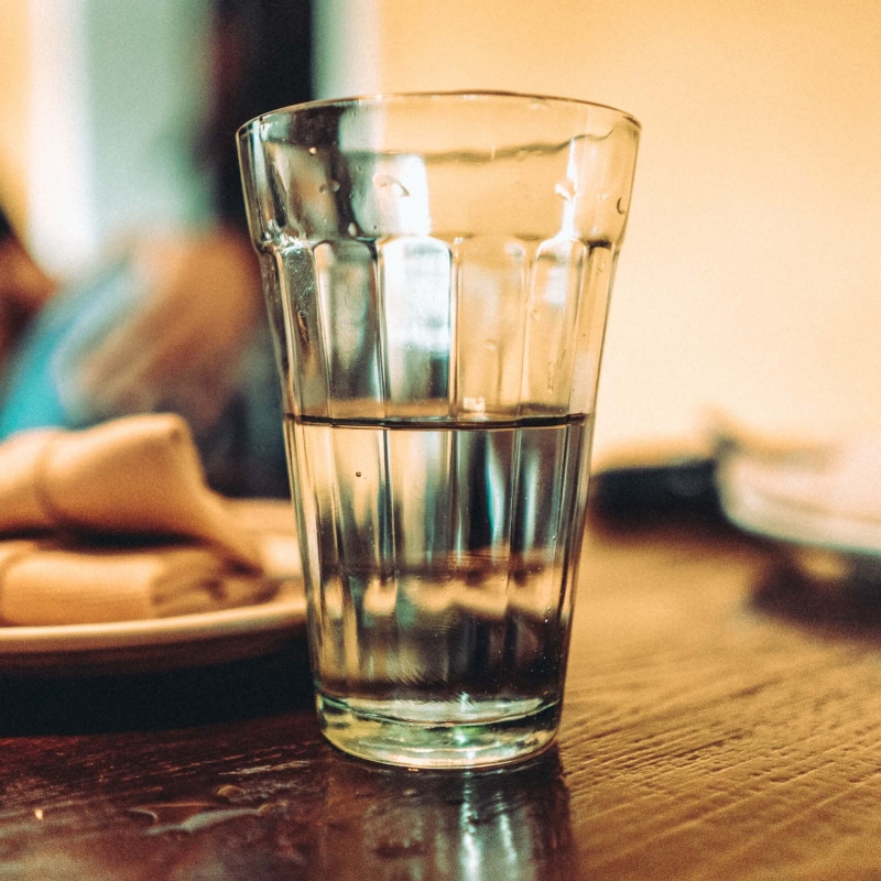 half a glass of water is on the wooden table.